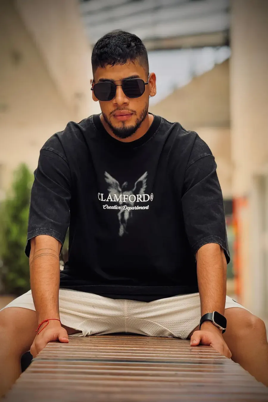 Hombre con camiseta oversize negra estampada Clamford sentado en una banca de madera