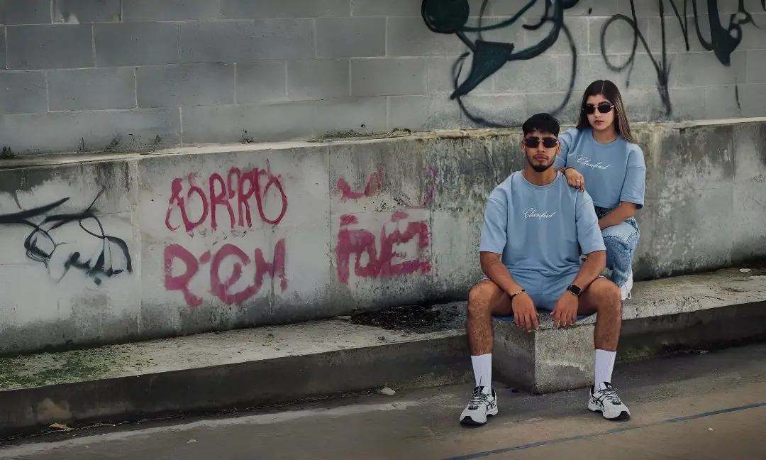 Pareja con camisetas oversize azul cielo sentada frente a un muro con graffiti